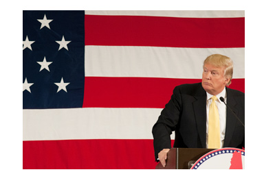 Donald Trump is standing at the podium with the american flag in the background. He has a look of concern on his face.