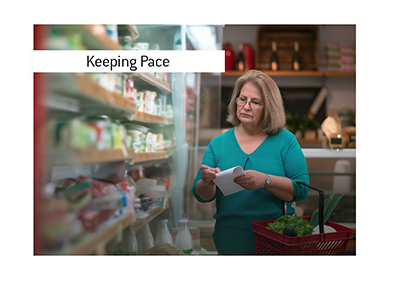 An older woman with  graying hair and glasses stands beside the refrigerated shelves of a neighborhood grocery store.