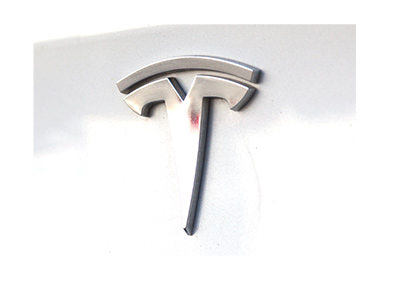 The Tesla logo as it was in the year 2018 on the back of a white car.  Zoomed in.