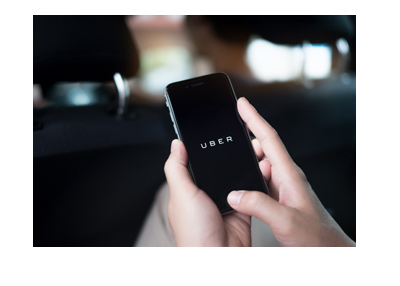 Woman is using the Uber application on her smartphone in the back of a car.  Black leather.